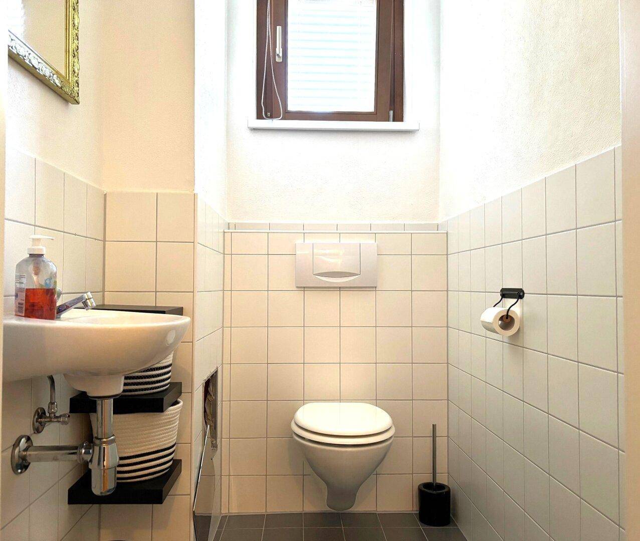 Kleines Gäste-WC mit wandmontierter Toilette, Waschbecken und Fenster.
