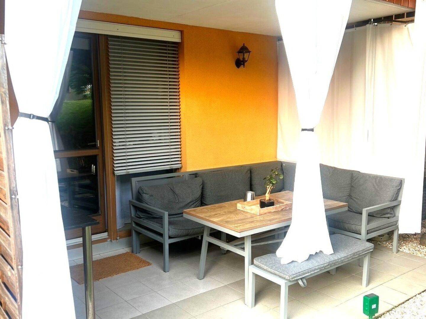 Gemütliche Terrasse mit Sitzmöbeln, Sonnenschutz und orangefarbener Wand, ideal zum Entspannen.