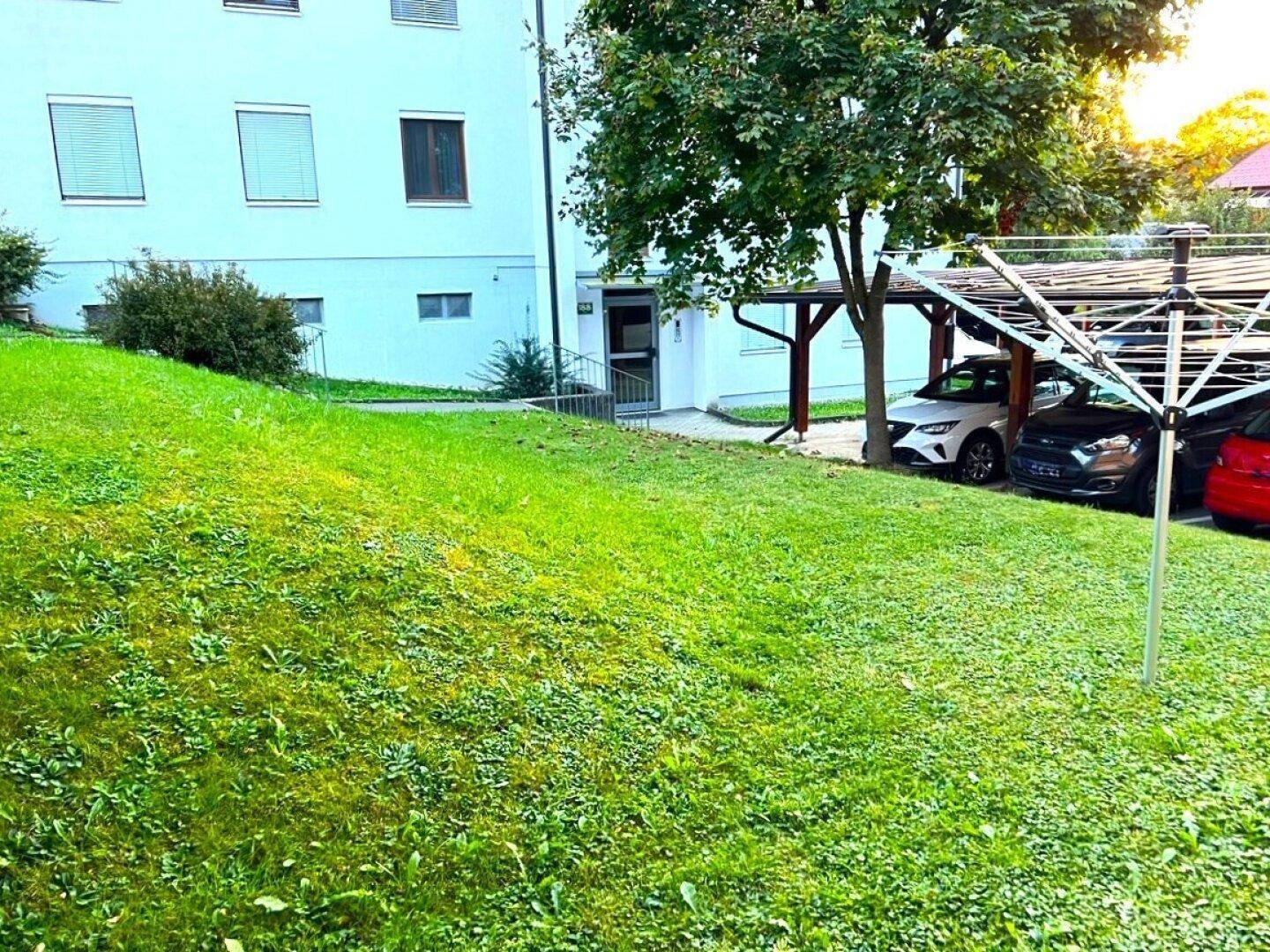 Außenansicht des Gebäudes mit gepflegtem Rasen und überdachten Parkplätzen.