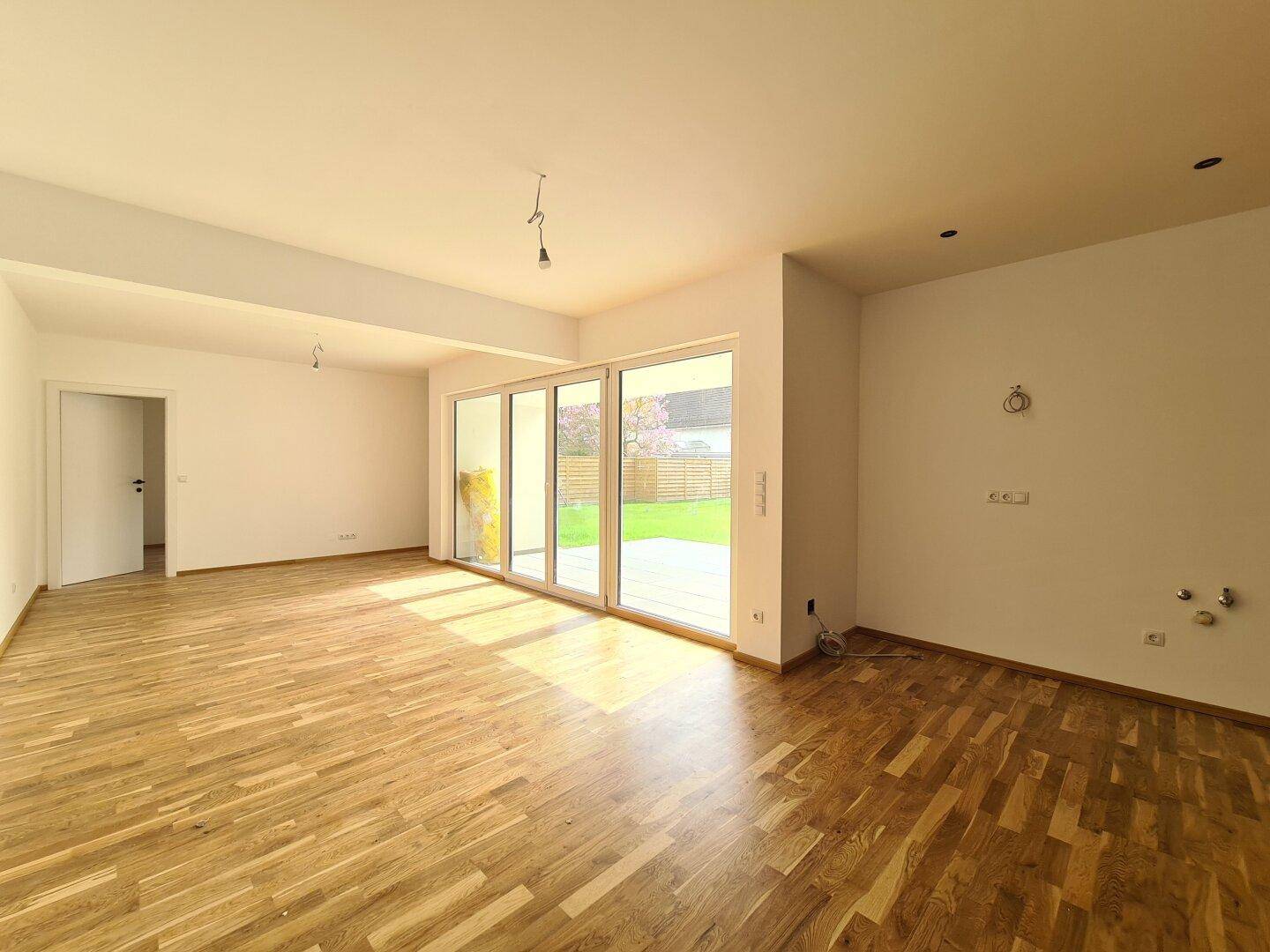 Heller, leerer Wohnbereich mit Eichenparkettboden und großen Fenstern zum Garten.