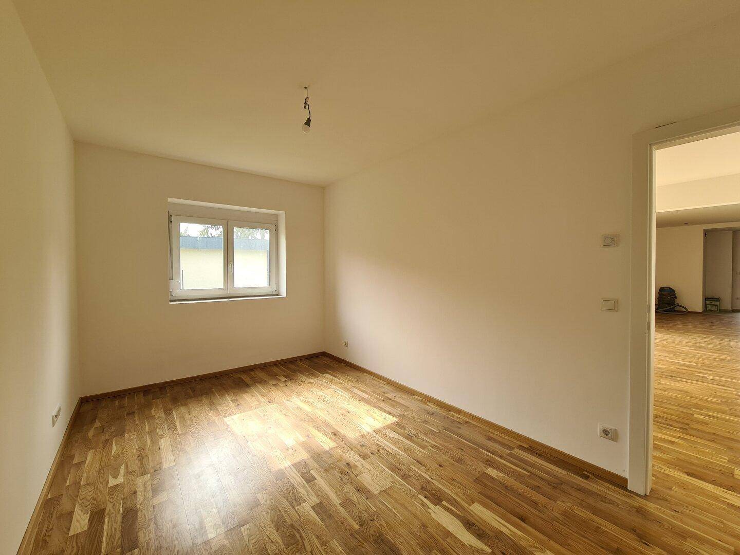 Leeres Zimmer mit hellem Eichenparkettboden und einem Fenster, ideal als Schlaf- oder Arbeitszimmer.