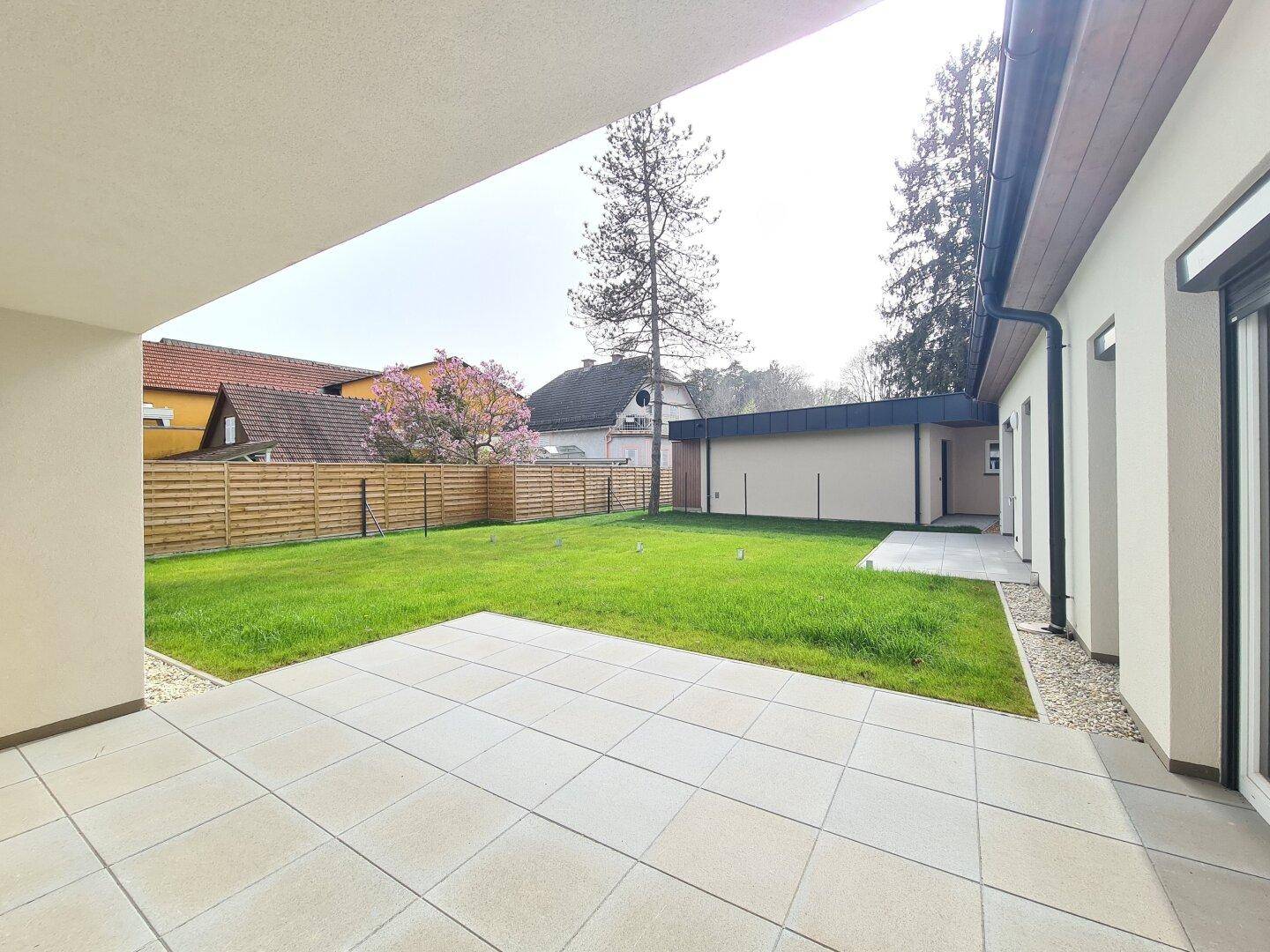 Großzügige, geflieste Terrasse mit angrenzendem Rasenbereich, ideal für Entspannung im Freien.