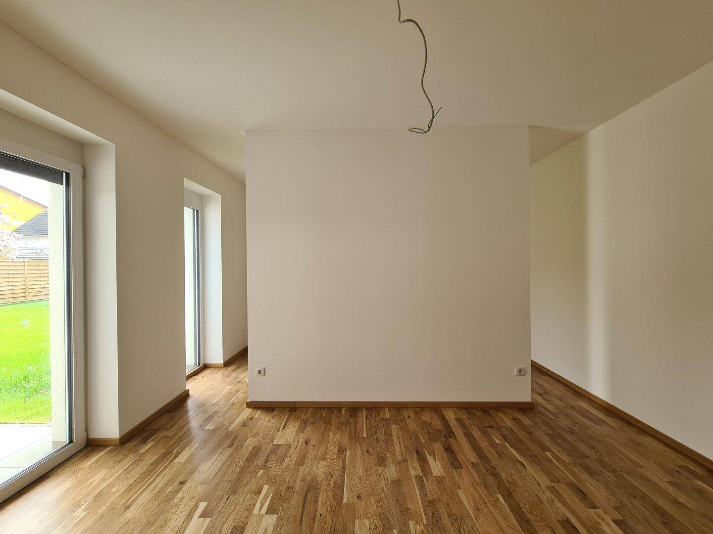 Großer, heller Raum mit Eichenparkett und bodentiefen Fenstern mit Blick ins Grüne.