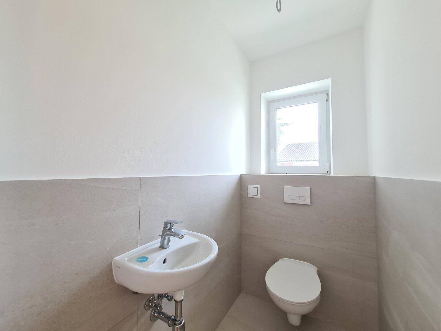 Helles Gäste-WC mit Fenster, modernem Waschbecken und wandhängender Toilette.