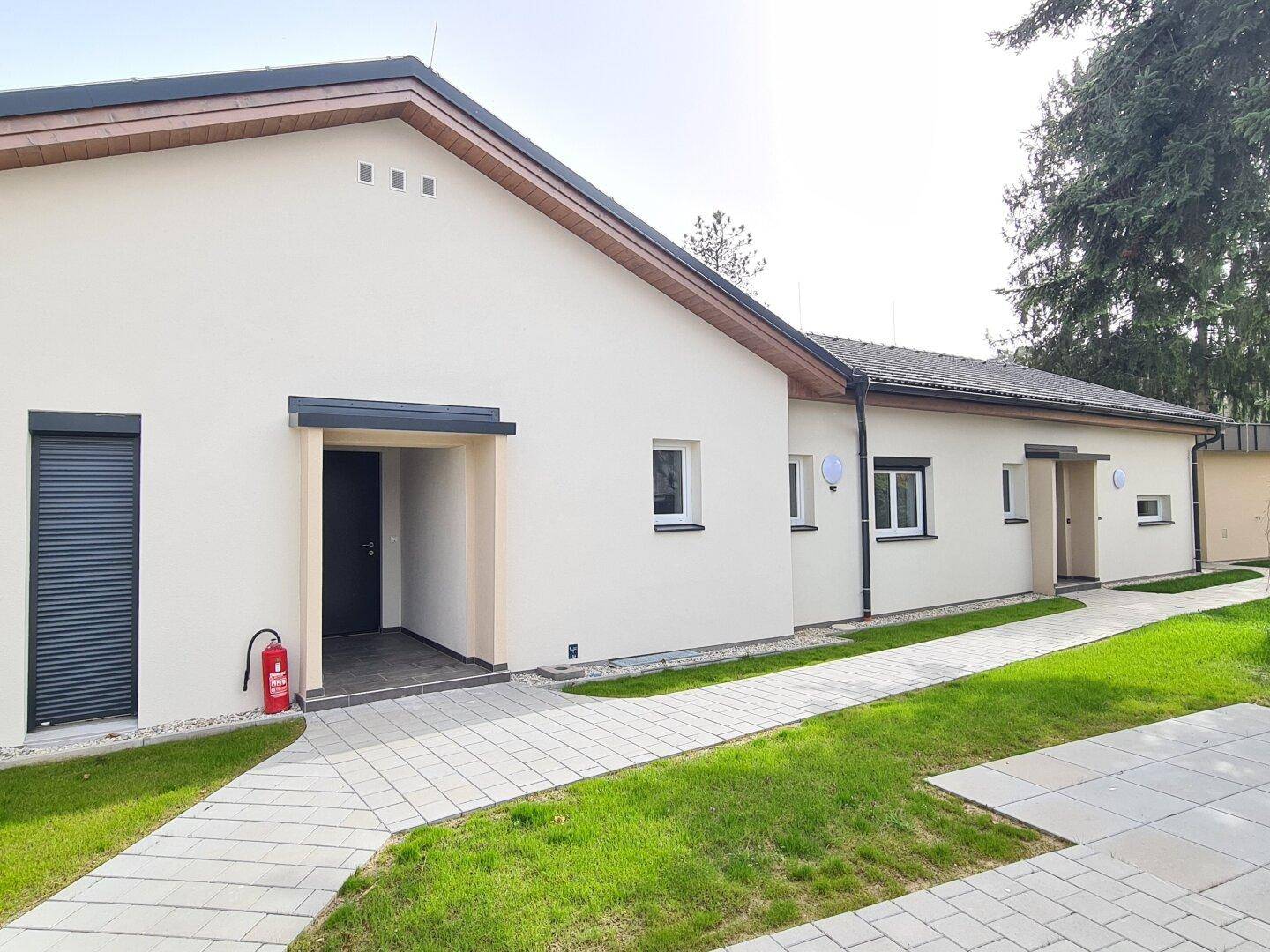 Eingangsbereich des modernen Neubaus mit gepflastertem Weg und Rollläden an den Fenstern.