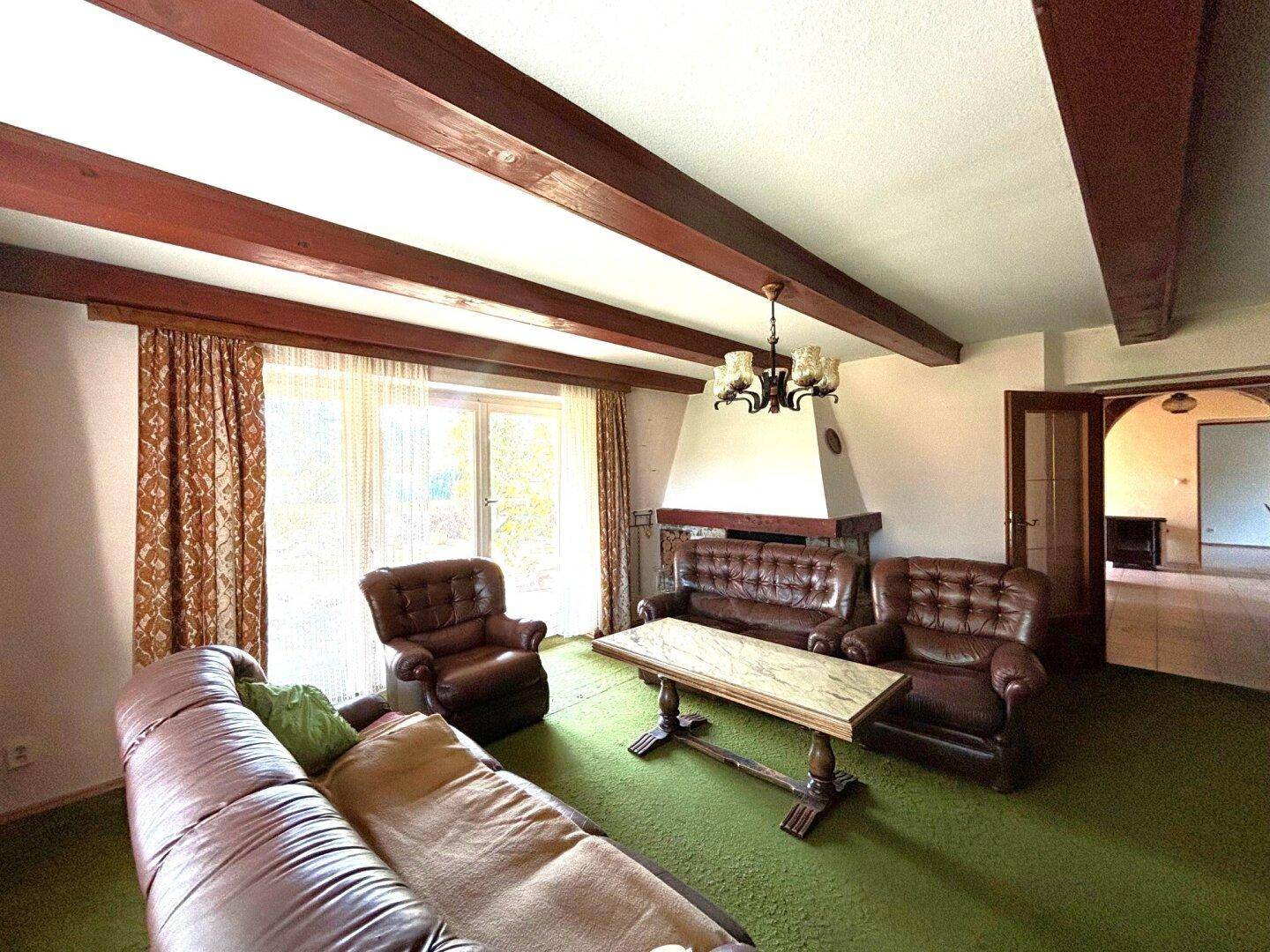 Gemütliches Wohnzimmer mit grüner Teppichboden, Ledersofas und sichtbaren Holzbalken an der Decke.