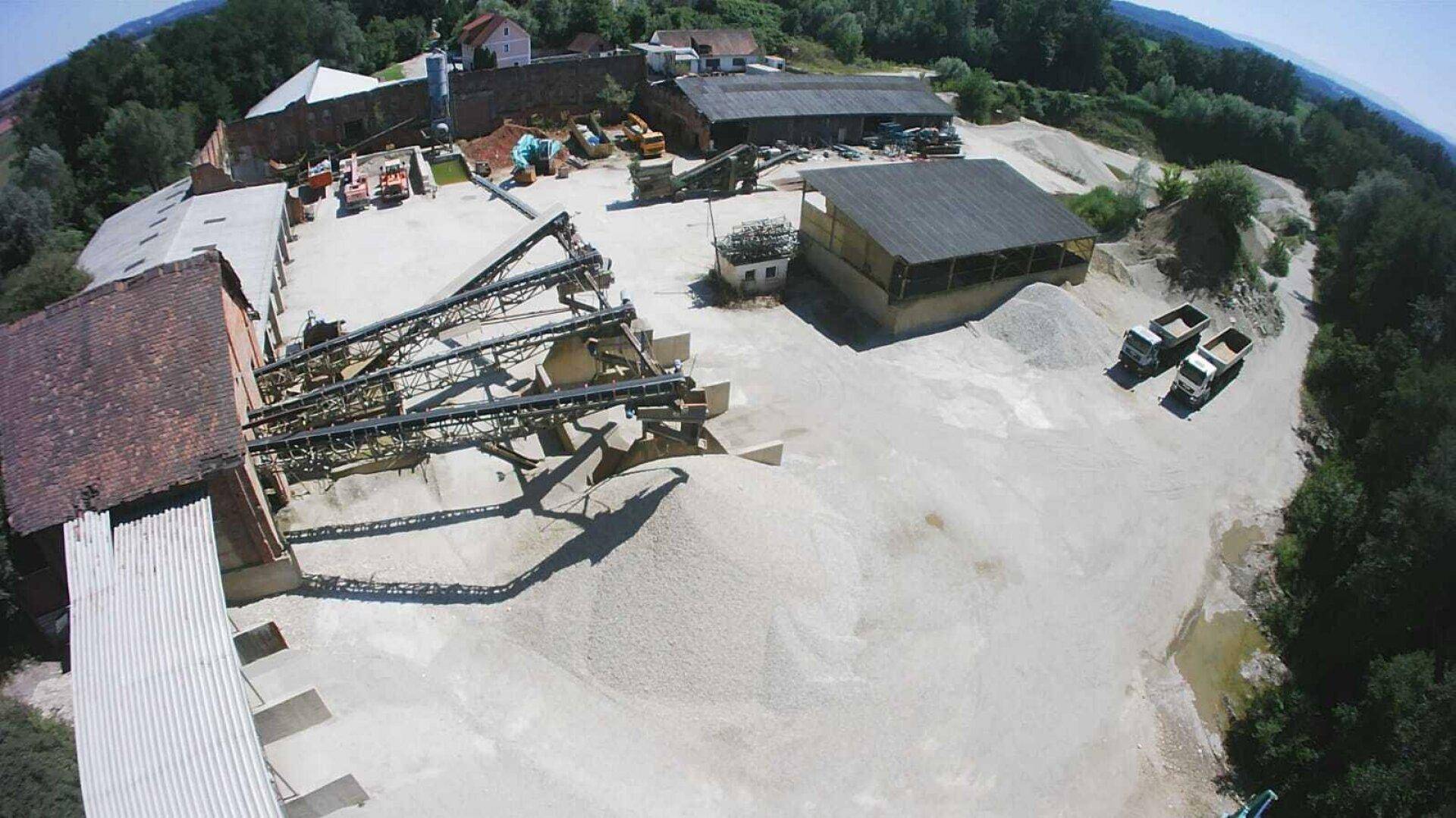 Übersicht aus der Luft der Kiesanlage mit Förderbändern, Lagerhallen und Lastwagen auf dem Gelände.