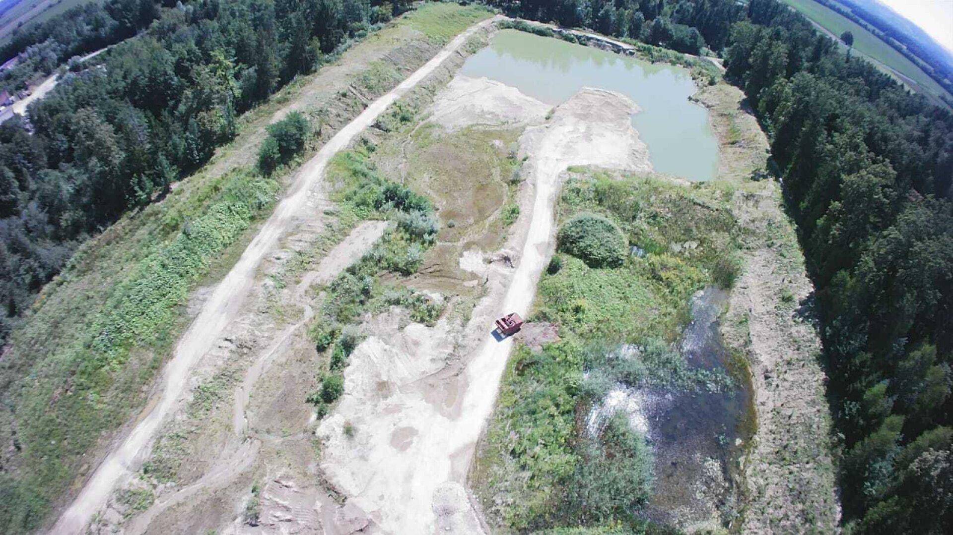 Luftaufnahme eines großen Abbaugebietes mit Wasserflächen und unbefestigten Wegen, umgeben von dichtem Wald.