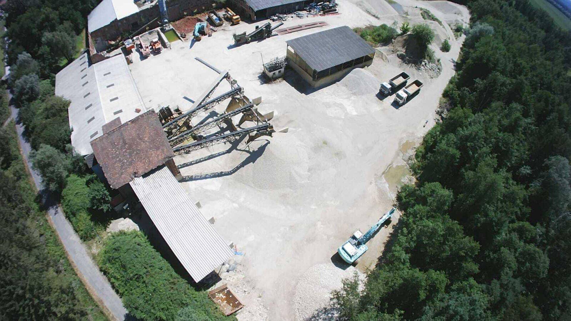 Blick von oben auf die Kiesaufbereitungsanlage mit großen Materialhaufen, Förderbändern und Arbeitsgeräten.