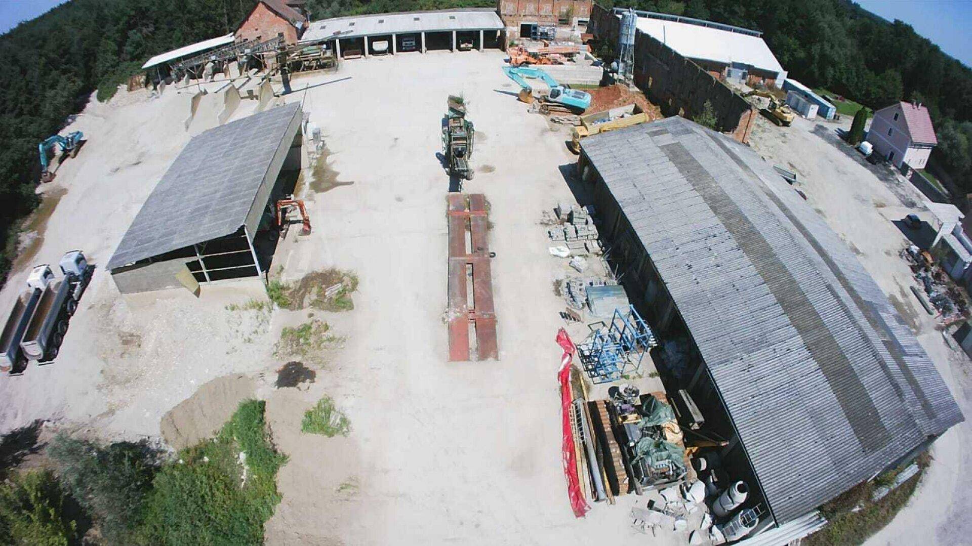 Übersicht aus der Luft des Betriebsgeländes mit großen Lagerhallen, Lastwagen und verschiedenen Geräten.