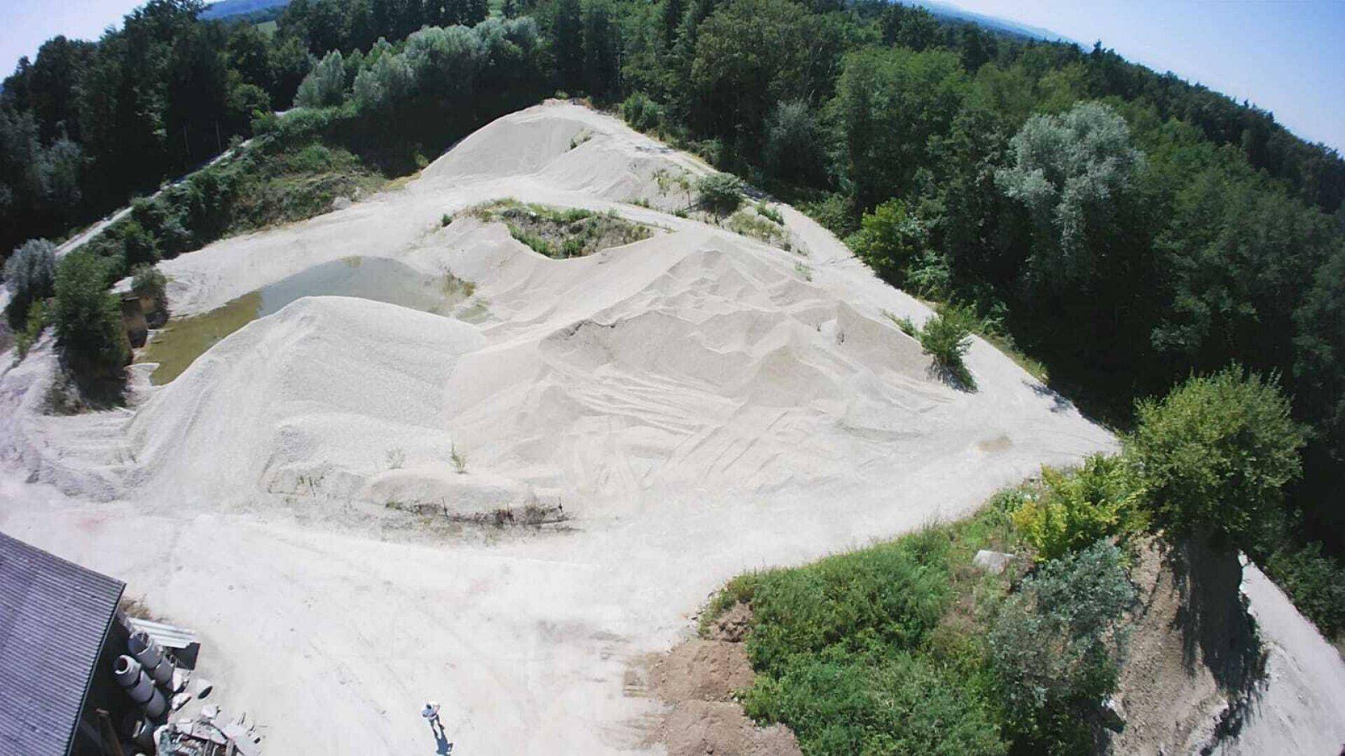 Luftaufnahme von imposanten Sandhügeln, die von dichtem Wald umgeben sind, unter klarem Himmel.