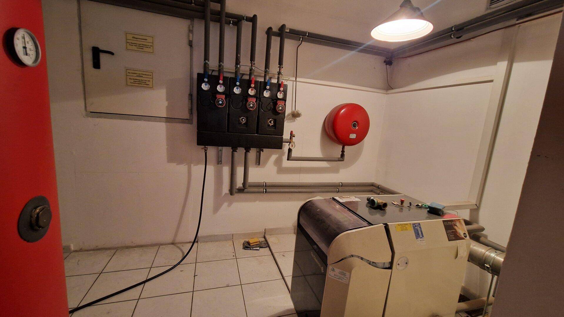 Heizraum im Keller mit technischen Installationen und Fliesenboden.