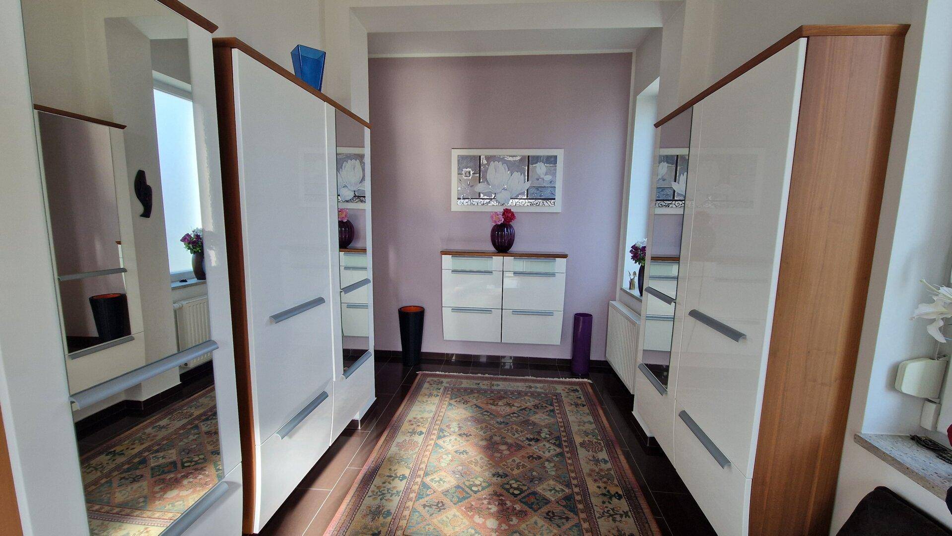 Heller Flur mit Spiegelschränken, Teppichboden und einer Kommode an der Wand.