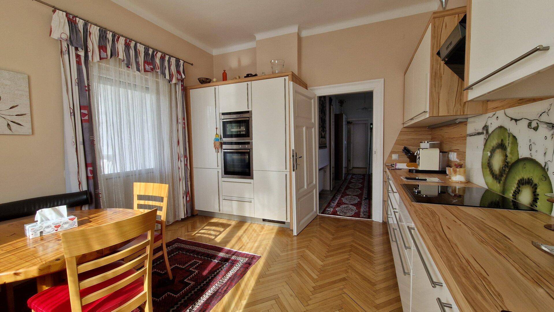 Geräumige Küche mit integrierten Geräten, Holzelementen und Zugang zu einem weiteren Raum.