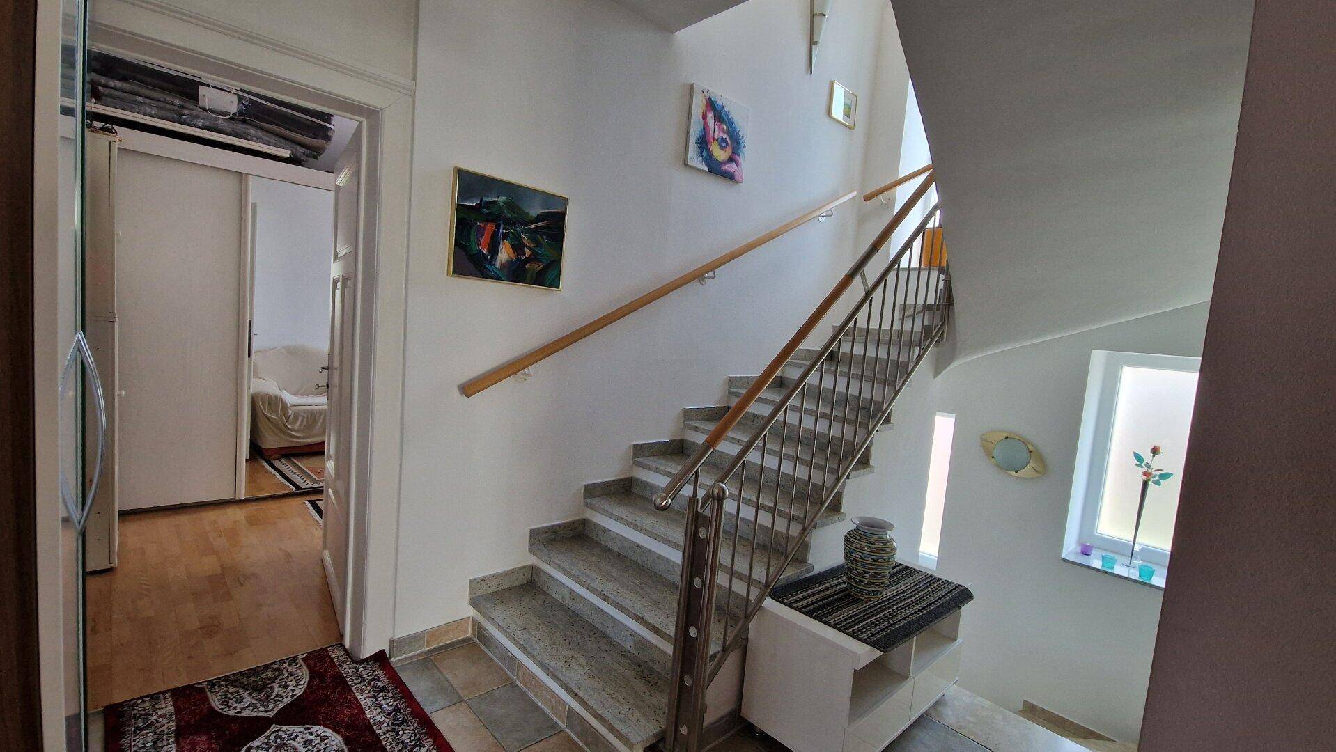 Treppenhaus mit Steinstufen, Metallgeländer und Kunstwerken an den Wänden.
