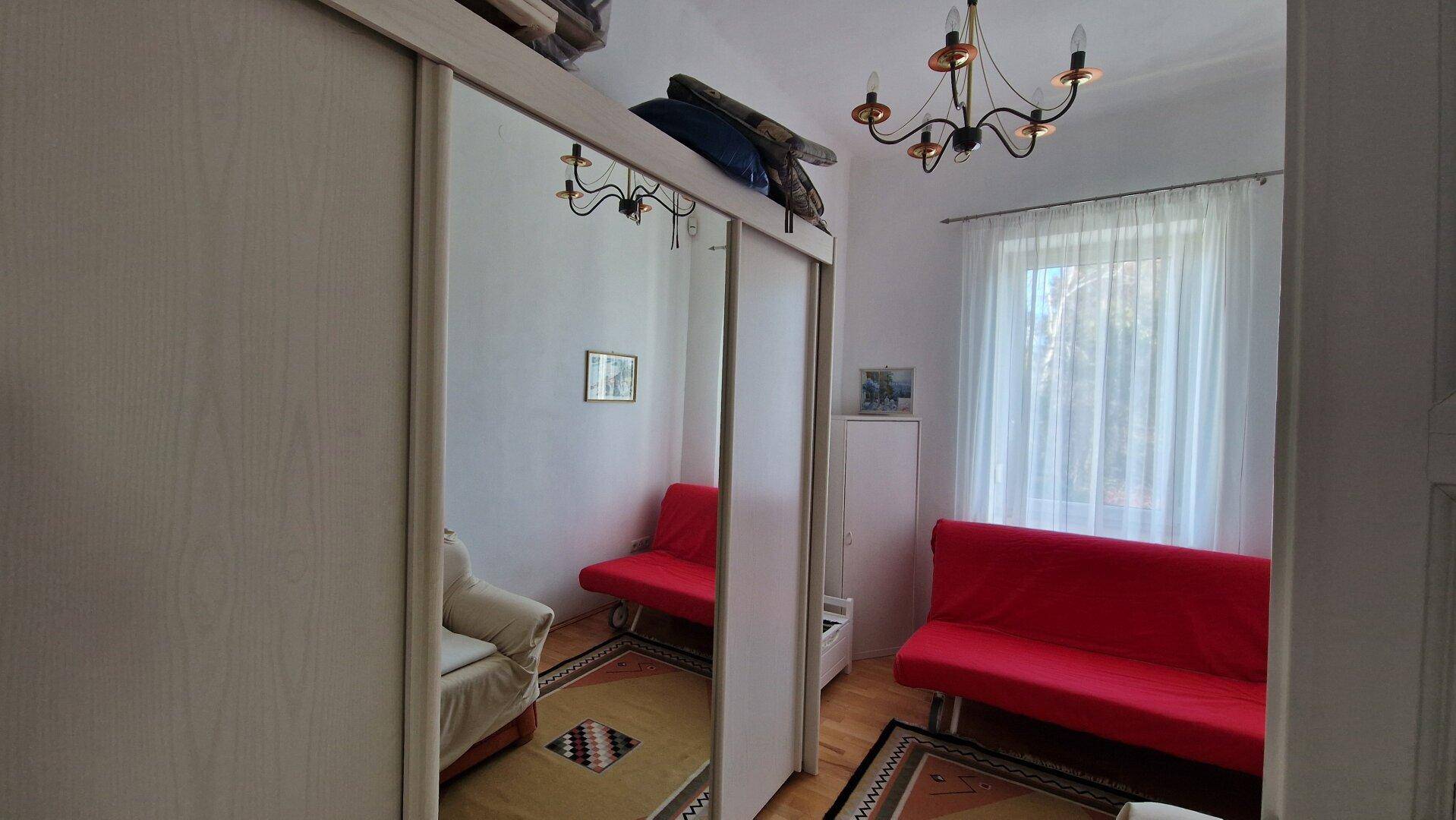Schlafzimmer mit rotem Sofa, Spiegelschränken und Parkettboden.