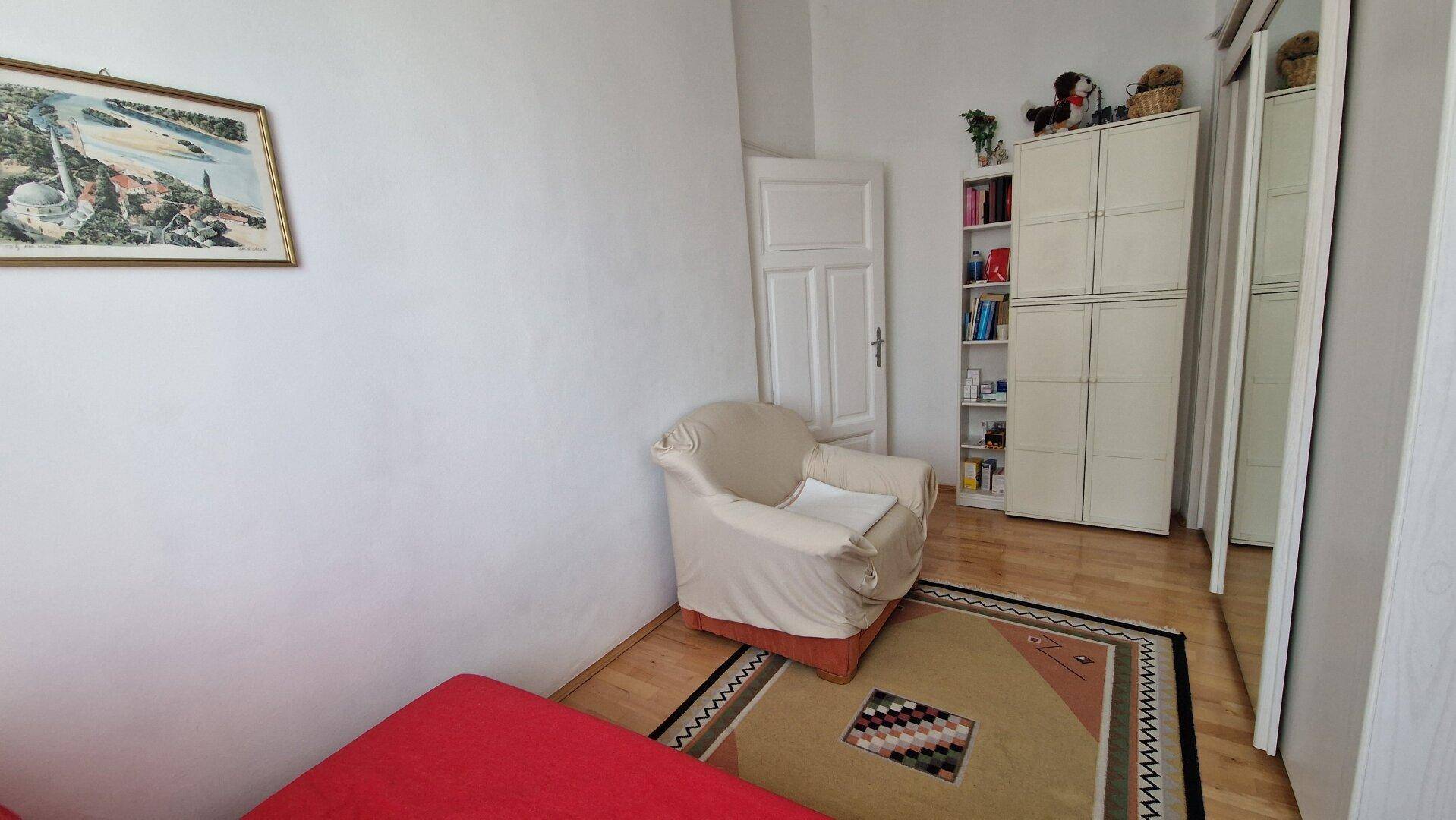 Schlafzimmer mit Einzelbett, Sessel und Parkettboden.