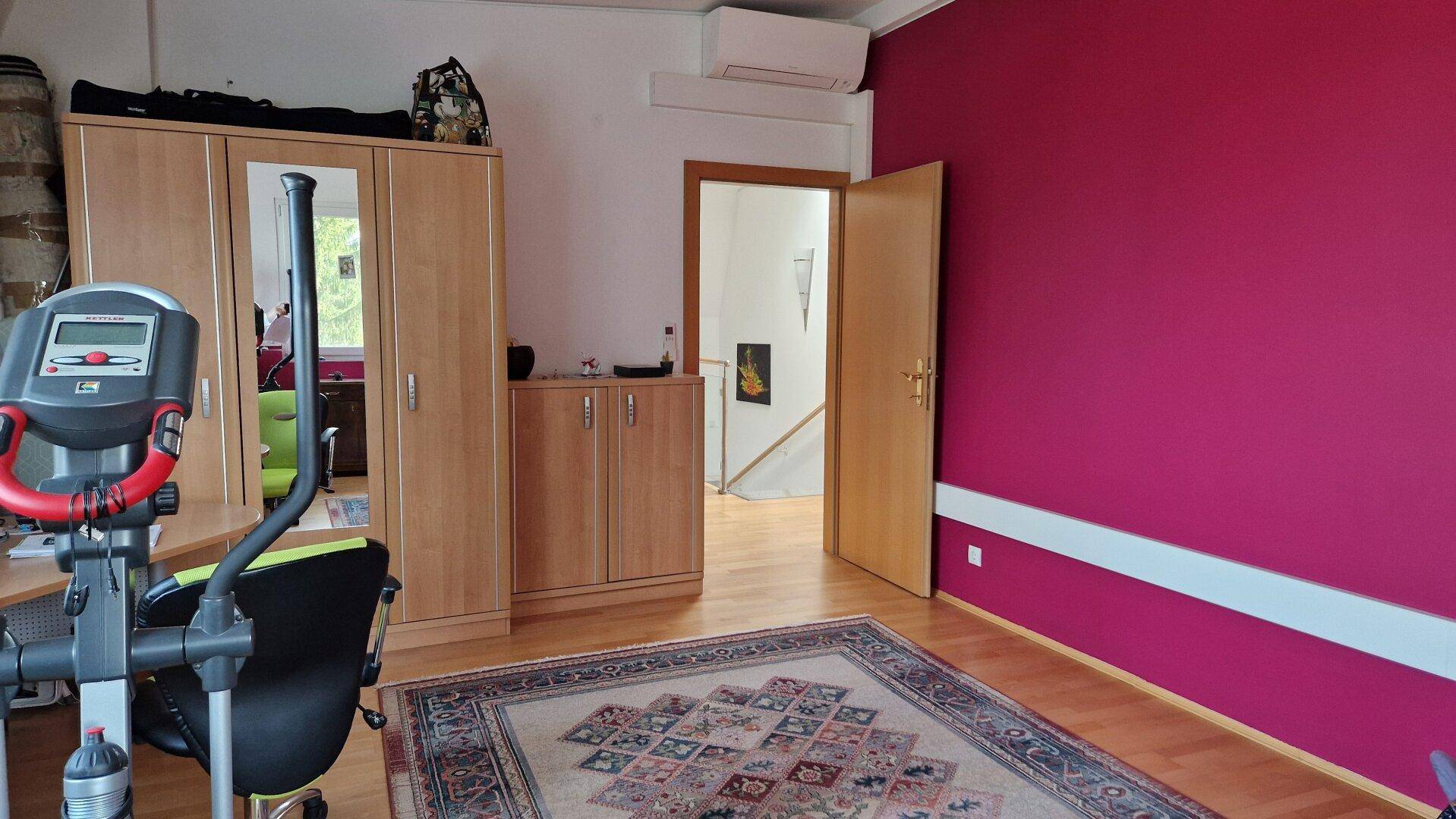 Arbeitszimmer mit Fitnessgerät, Schrank und farbiger Wandgestaltung.