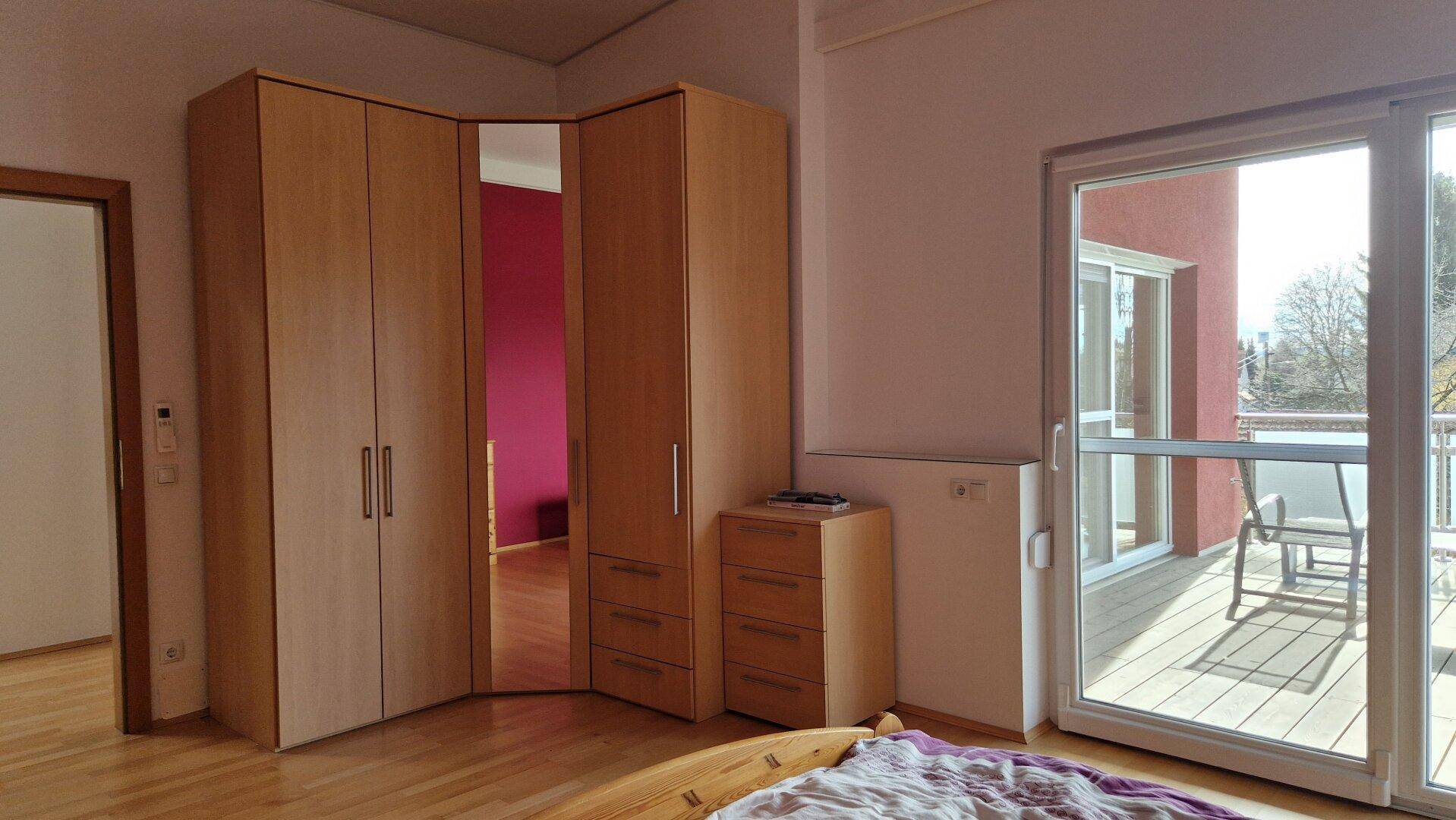 Schlafzimmer mit Eckkleiderschrank, Holzboden und Zugang zum Balkon.