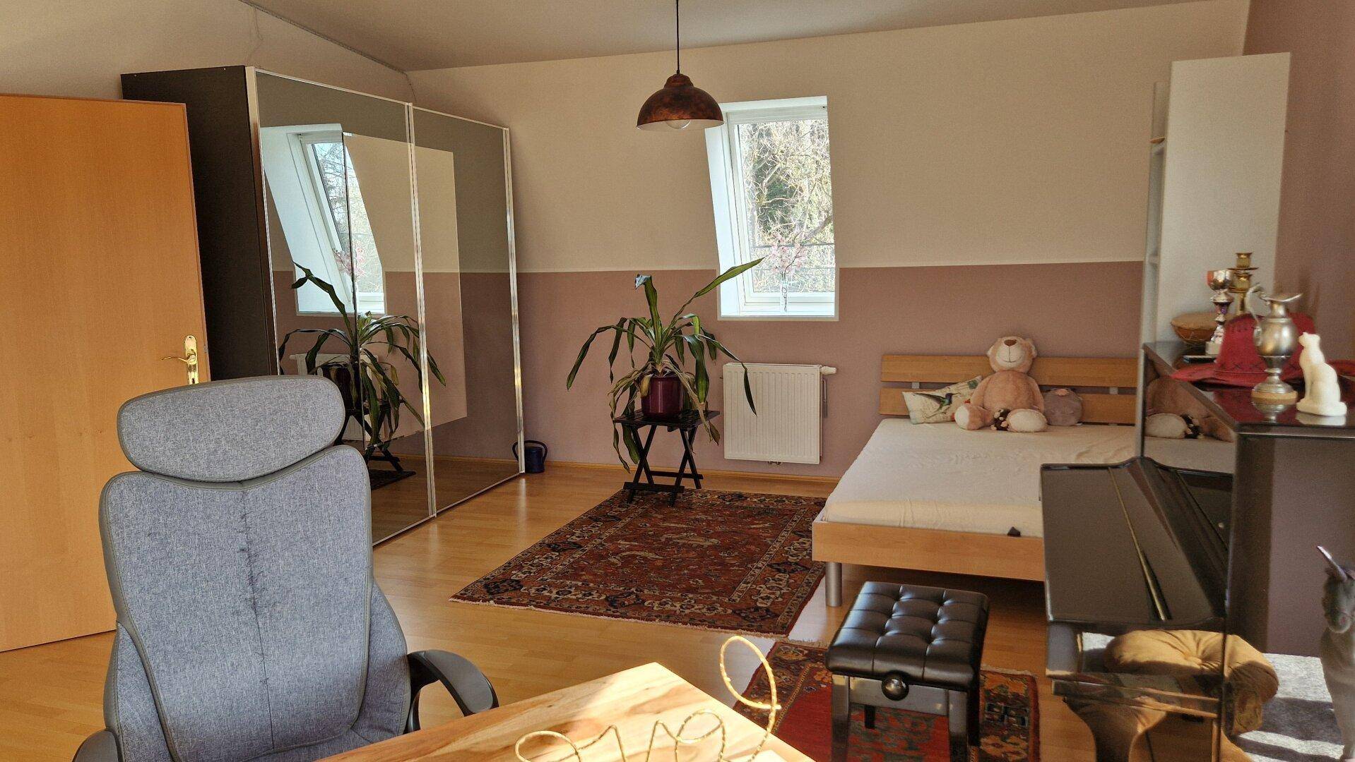 Schlafzimmer mit Bett, Klavier und Spiegelschränken.