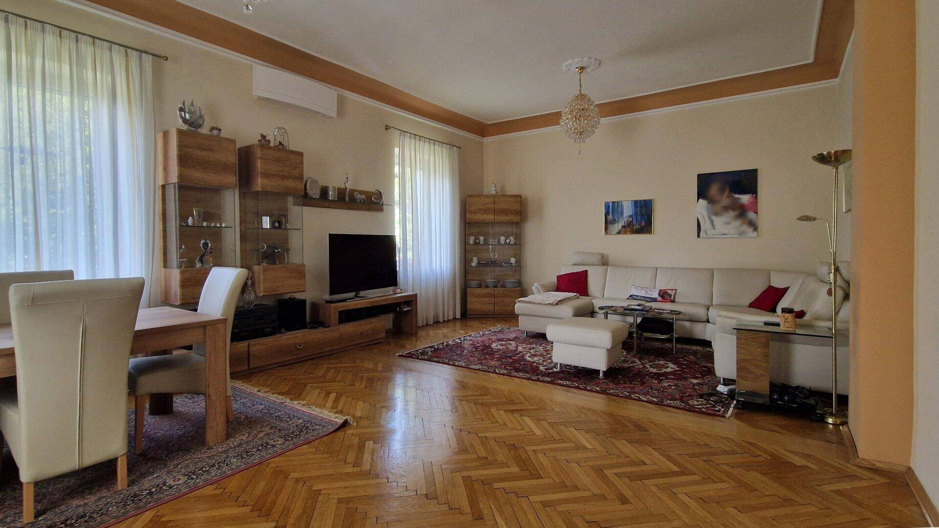 Geräumiger Wohn-Essbereich mit Parkettboden, beiger Couch und Kronleuchter.