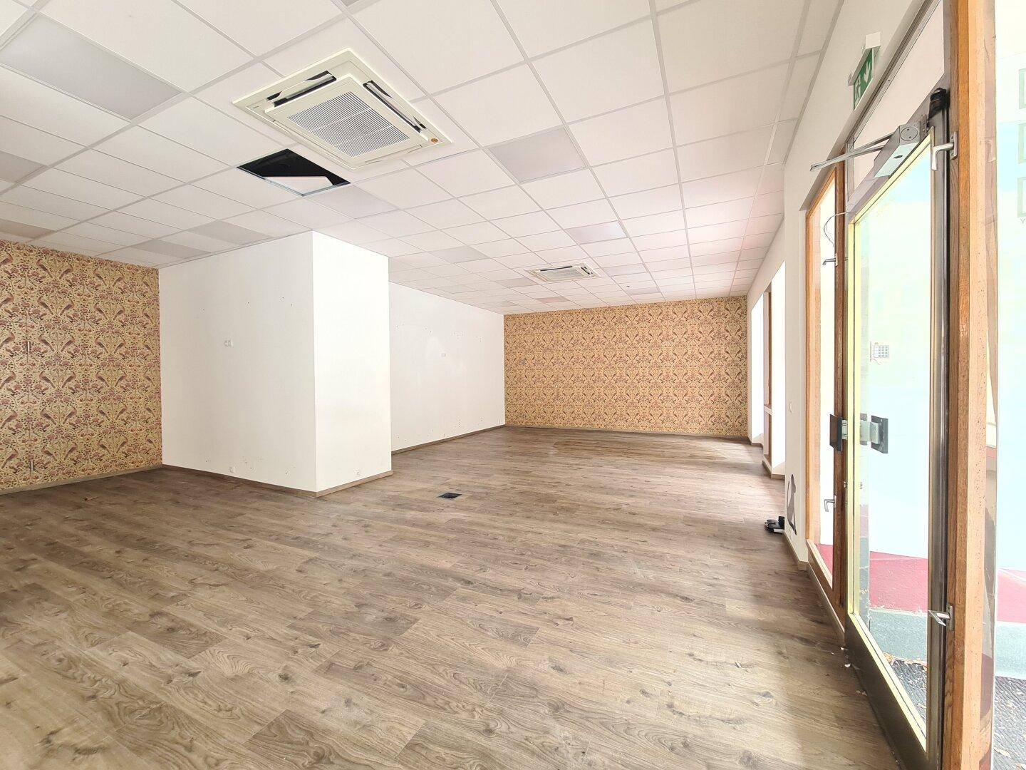 Großer Geschäftsraum mit Laminatboden, gemusterter Tapete an den Wänden und abgehängter Decke.