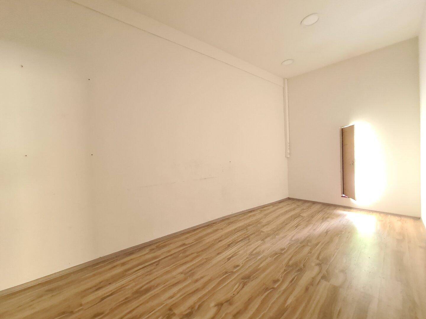 Kleiner, leerer Raum mit hellem Laminatboden und einer Lichtquelle an der Seitenwand.