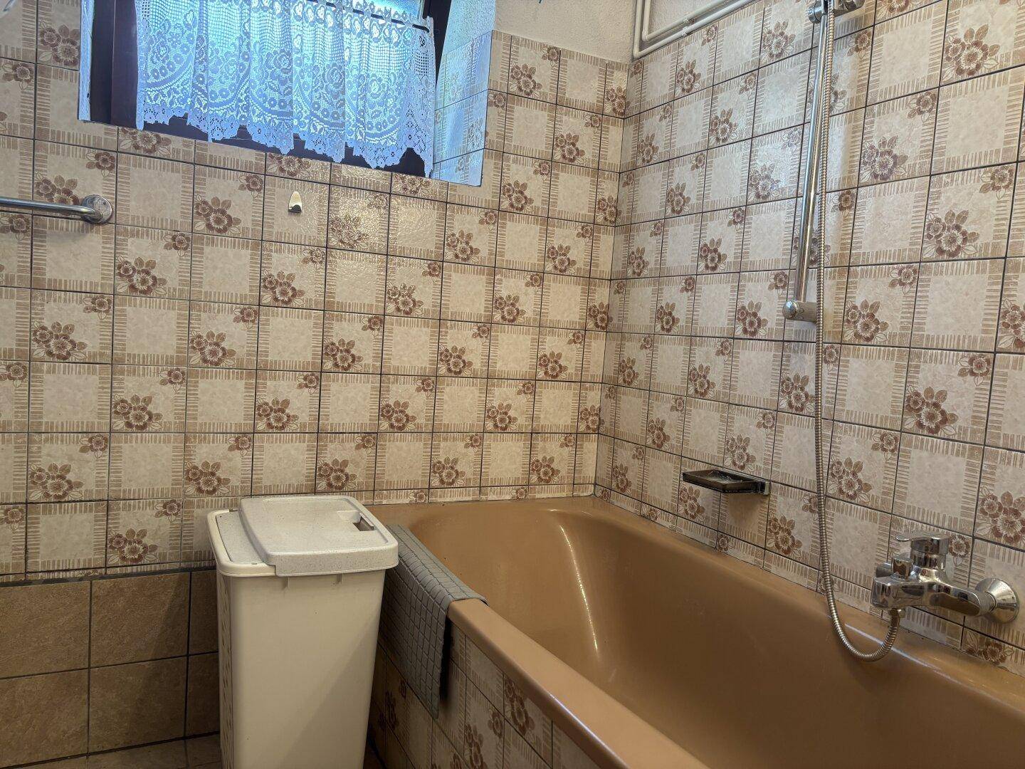 Badezimmer mit brauner Badewanne und gemusterten Fliesen im 80er-Jahre-Stil.