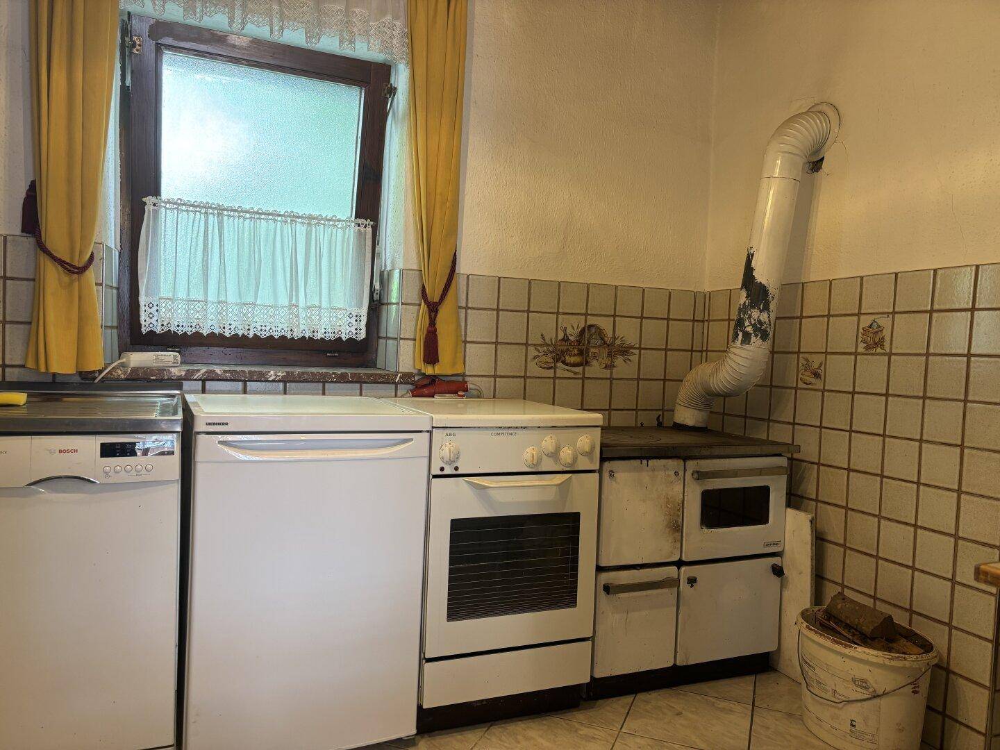 Traditionelle Küche mit Holzofen, Elektroherd und Spülmaschine unter einem Fenster.