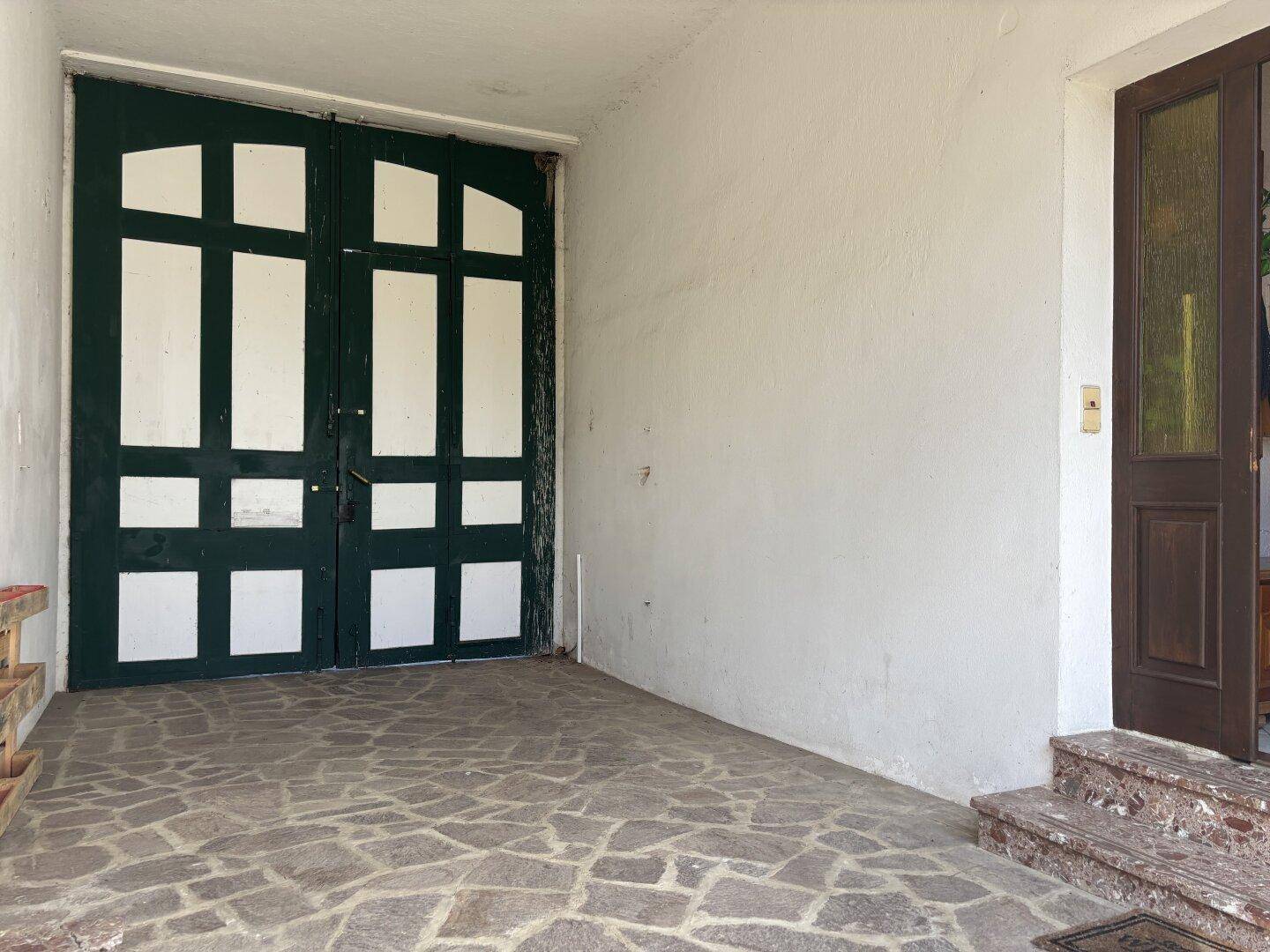 Eingangsbereich mit großen, traditionellen Holztüren und robustem Steinboden.