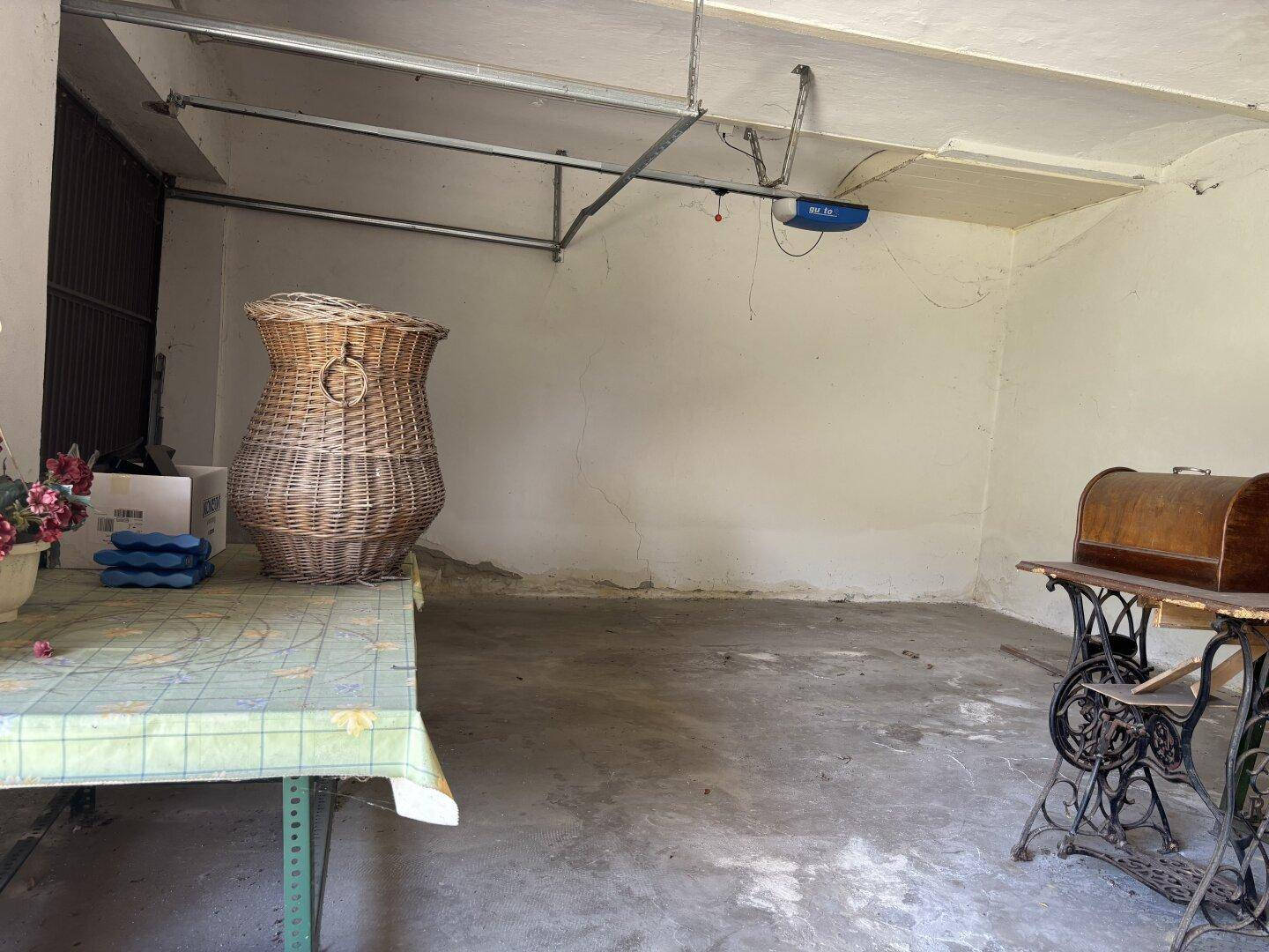 Geräumige Garage mit Betonboden und einem alten Nähtisch sowie einem großen Korb.