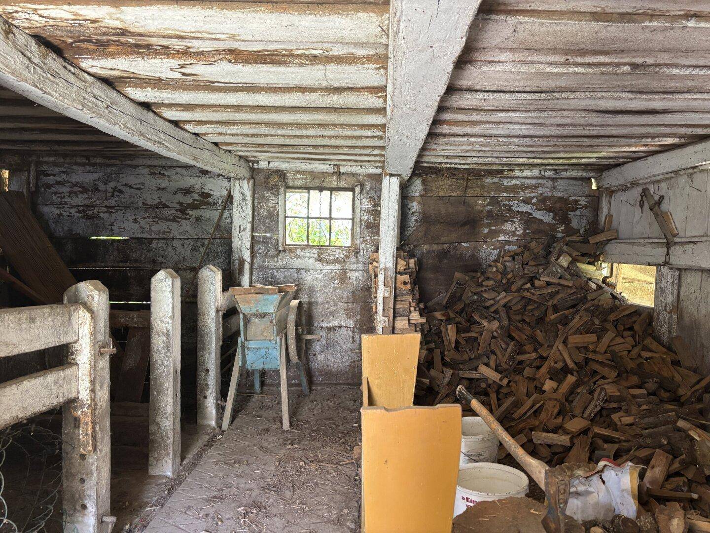 Alter Stall oder Schuppen mit Holzbalken, einem Fenster und einem großen Holzstapel.