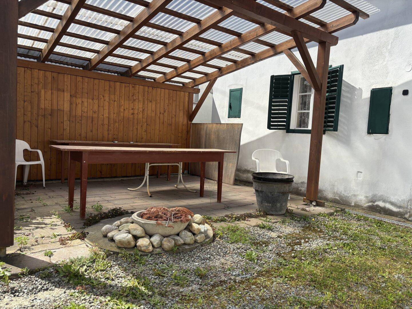 Überdachte Terrasse mit Holztisch und Sitzgelegenheiten, ideal für Mahlzeiten im Freien.