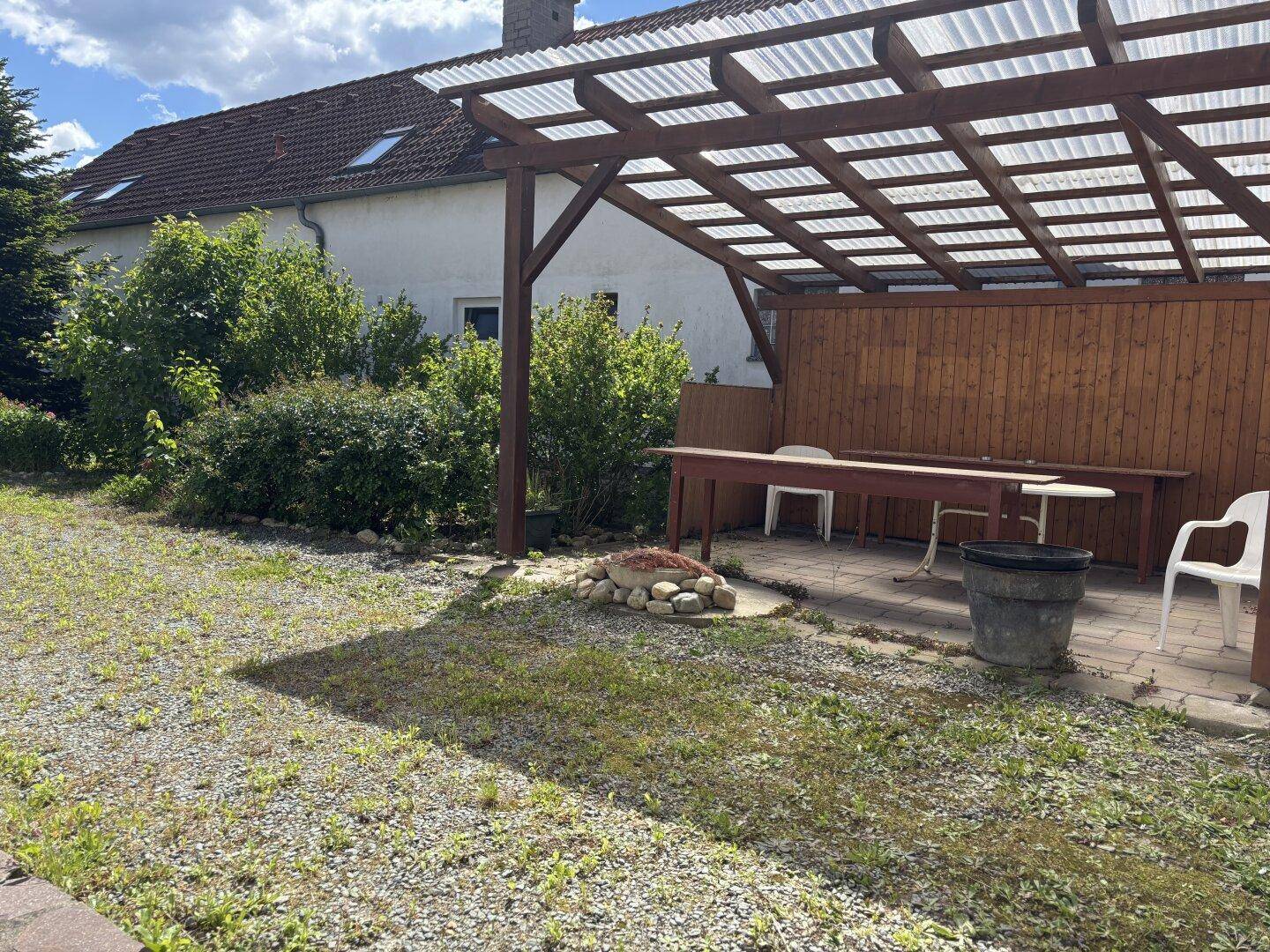 Überdachte Terrasse mit Holzbalken und Gartenbereich, ideal für entspannte Stunden im Freien.