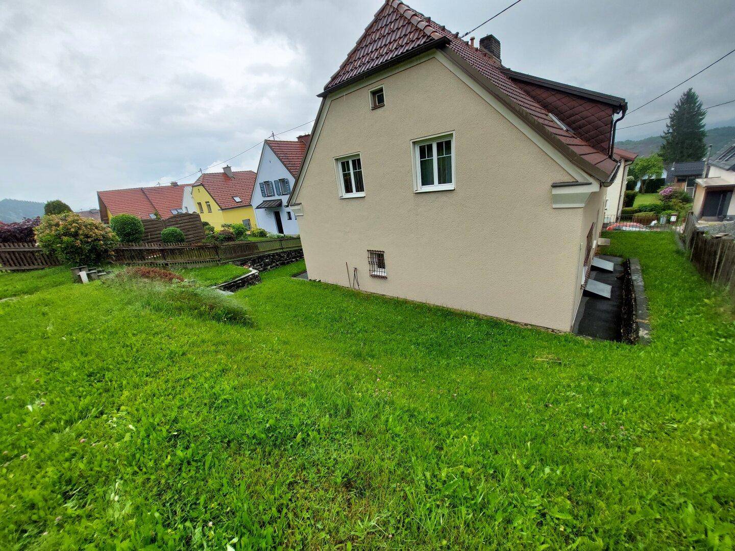 Seitenansicht des Hauses mit grünem Rasen und leichter Hanglage.