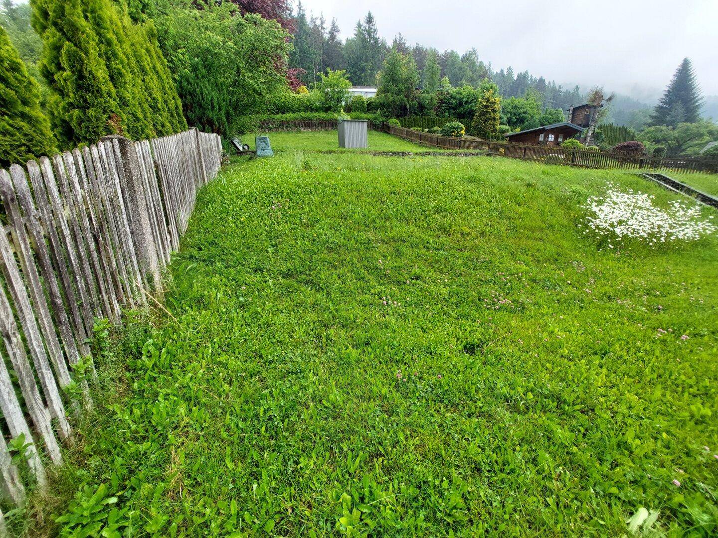 Großer, gepflegter Gartenbereich mit Rasenfläche und Holzzaun, umgeben von Bäumen.