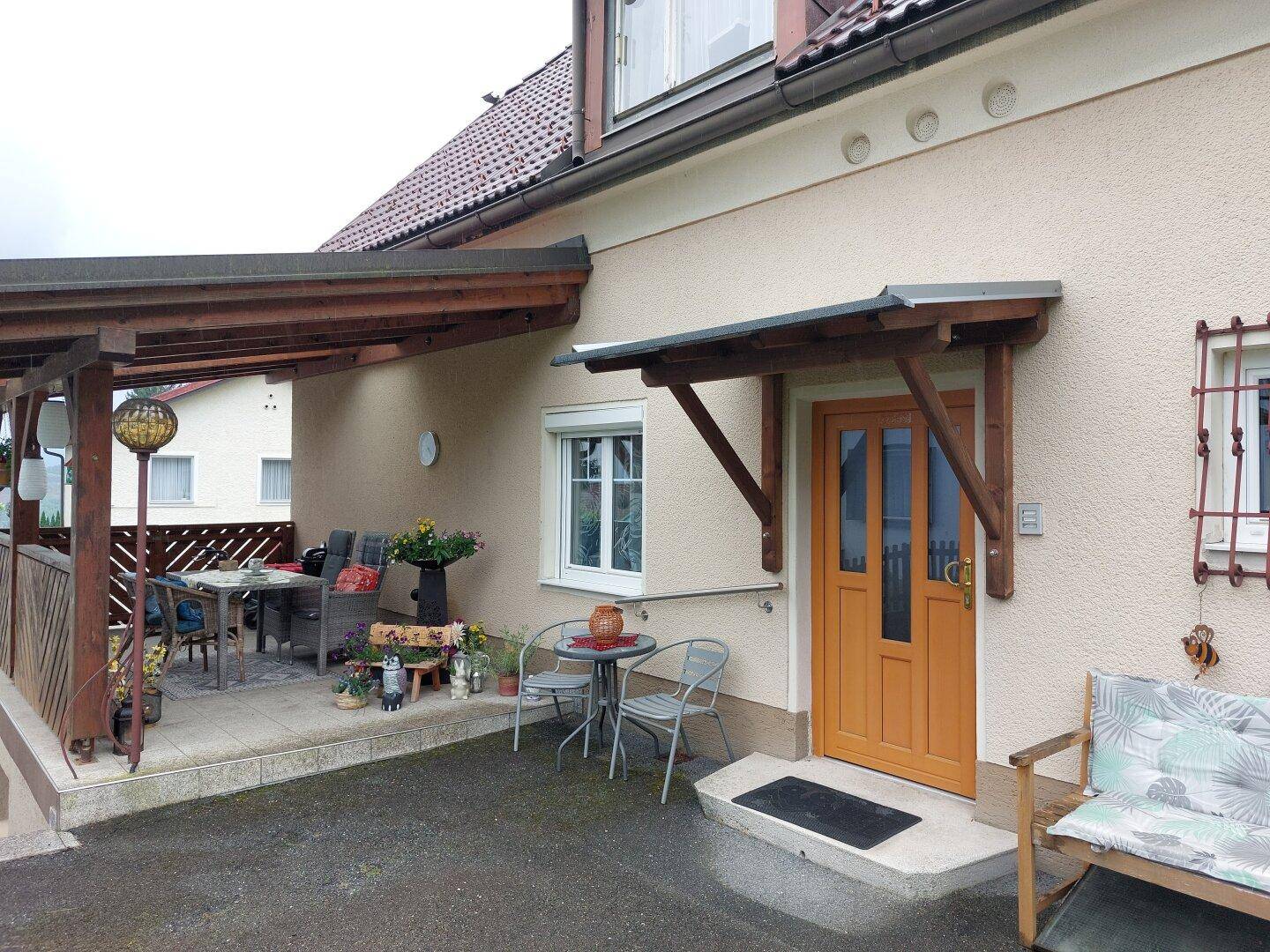 Eingangsbereich des Hauses mit überdachter Terrasse und Sitzgelegenheiten im Freien.