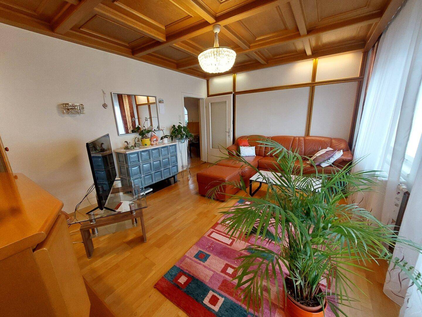 Gemütliches Wohnzimmer mit Holzkassettendecke, Parkettboden und Ledersofa.