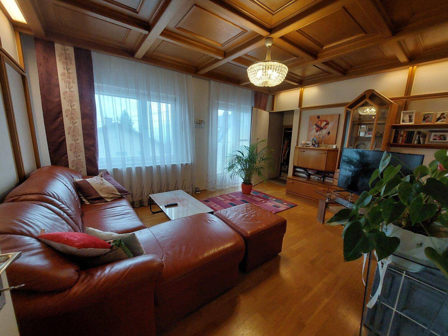 Wohnzimmer mit Holzkassettendecke, bequemer Ledercouch und Blick nach draußen.