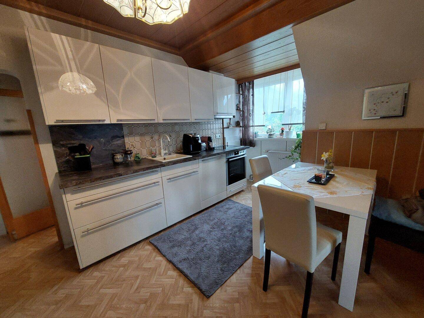 Moderne Küche mit weißen Hochglanzfronten, Essbereich und Dachschräge.