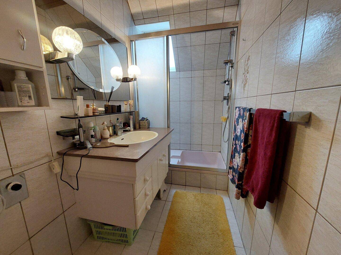 Gefliestes Badezimmer mit Dusche, Waschbecken und Dachfenster für natürliches Licht.