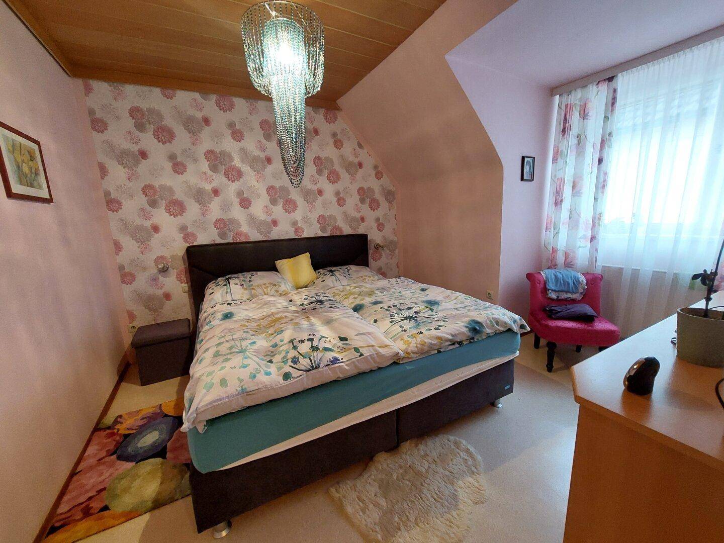 Schlafzimmer mit Doppelbett, floraler Tapete und Dachschräge, gemütlich eingerichtet.