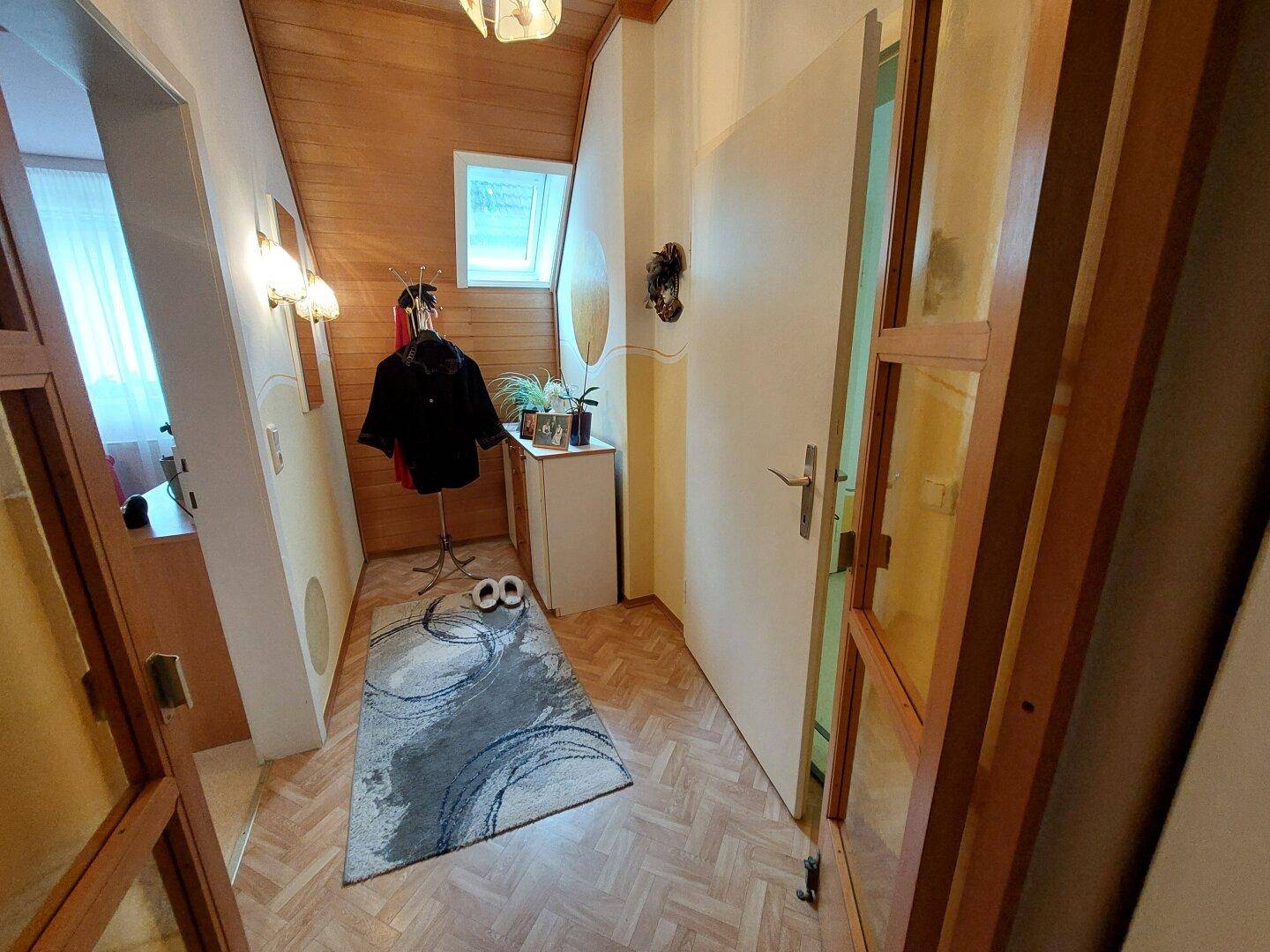 Heller Flur mit Holzverkleidung, Parkettboden und Garderobe im Dachgeschoss.