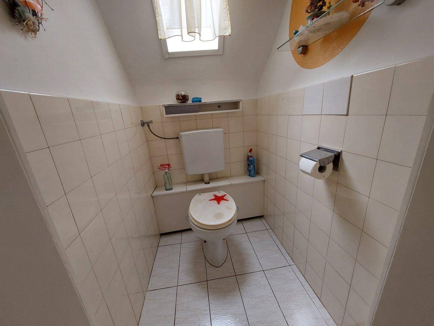 Kleines Gäste-WC mit Fliesen, Toilette und Dachfenster für Belüftung.