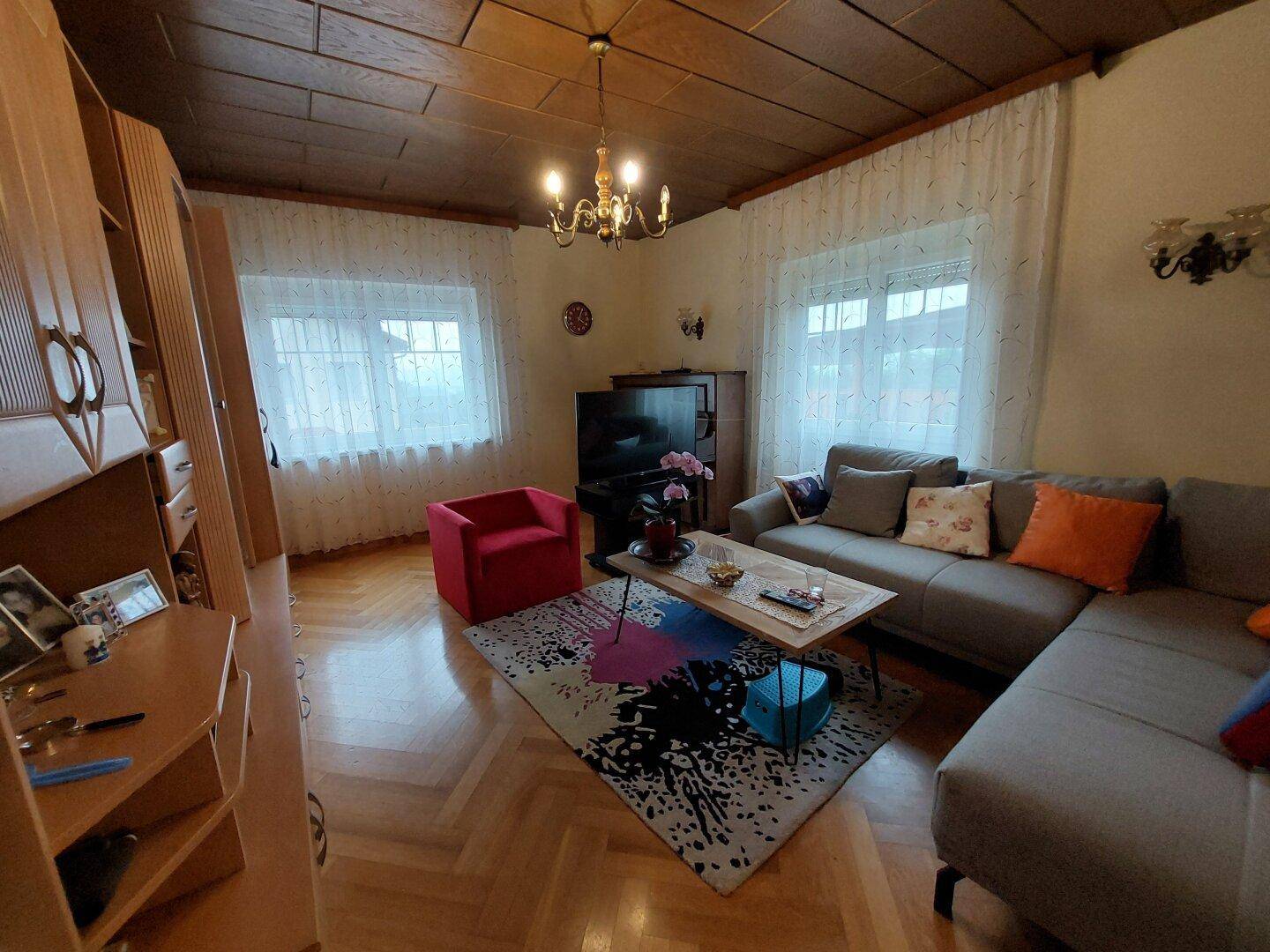 Geräumiges Wohnzimmer mit Holzkassettendecke, Parkettboden und gemütlicher Sitzecke.