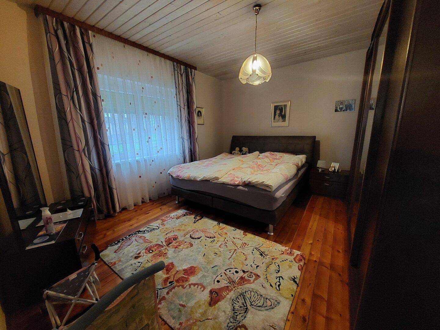 Schlafzimmer mit Doppelbett, Holzdecke und Parkettboden, gemütlich eingerichtet.