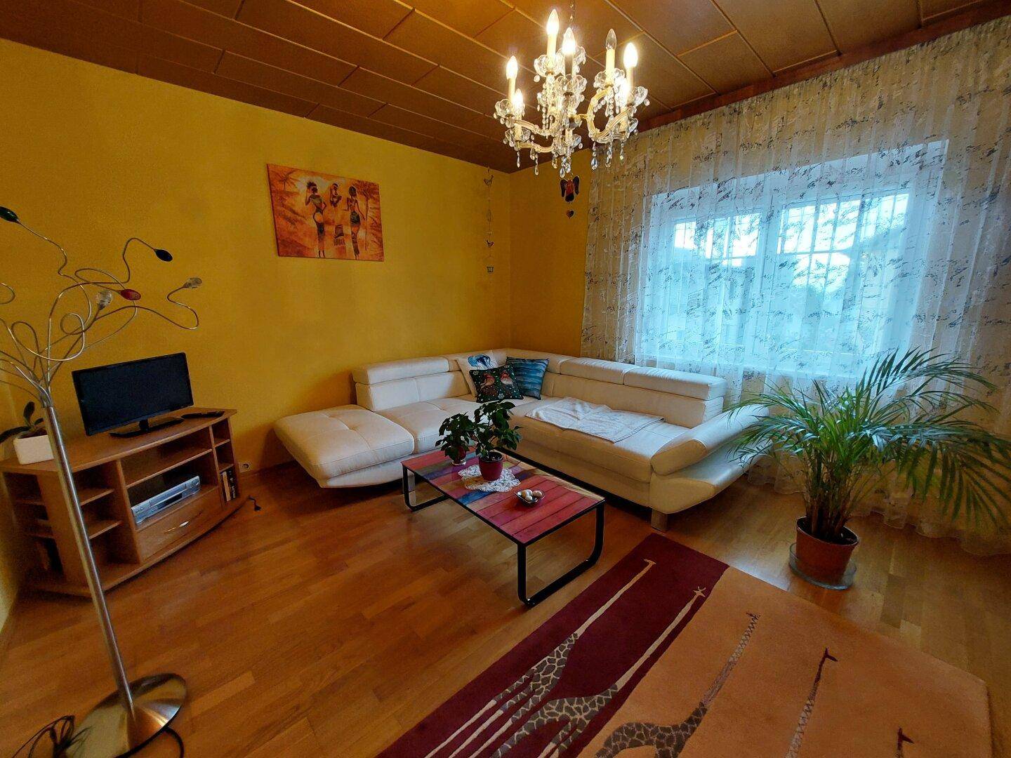 Geräumiges Wohnzimmer mit heller Ledercouch, Holzkassettendecke und Parkettboden.