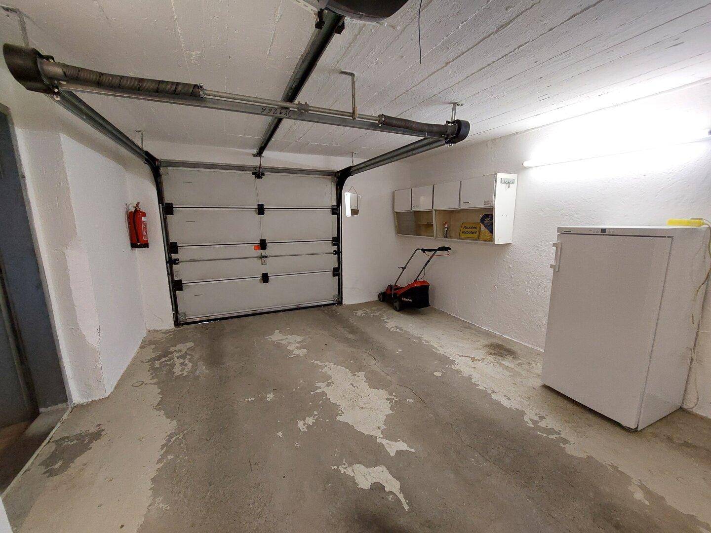 Helle Garage mit Sektionaltor, Stauraum und Platz für Gartengeräte sowie einen Gefrierschrank.