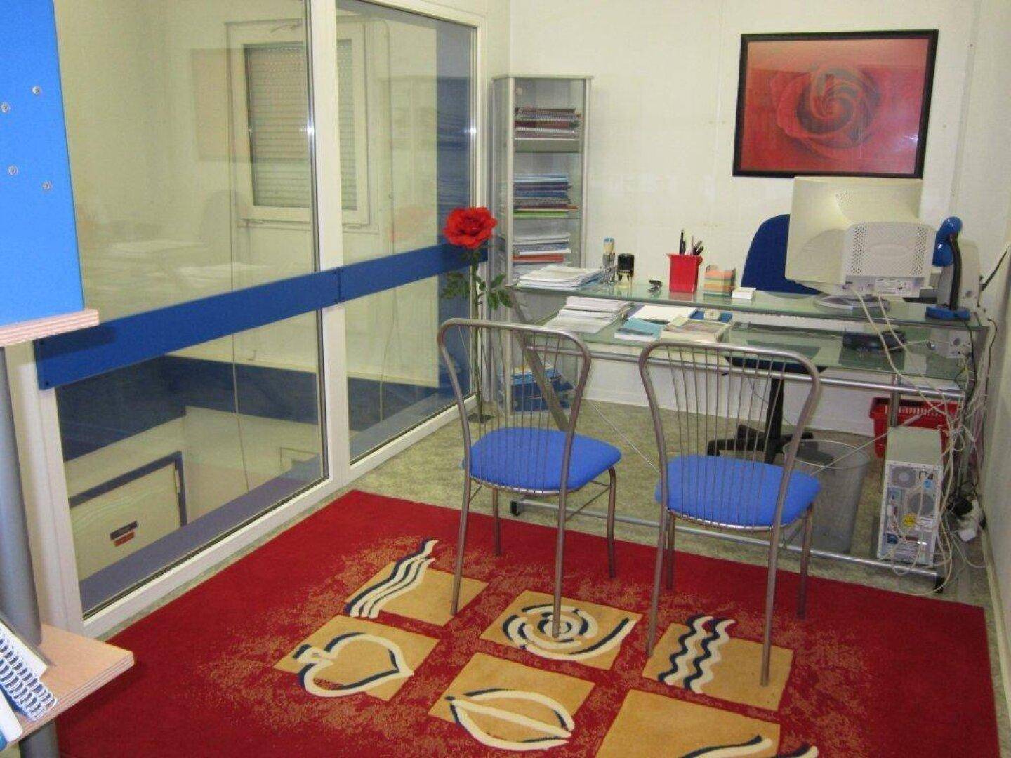 Modernes Büro mit Glastrennwand, Schreibtisch, Stühlen und einem auffälligen roten Teppich.