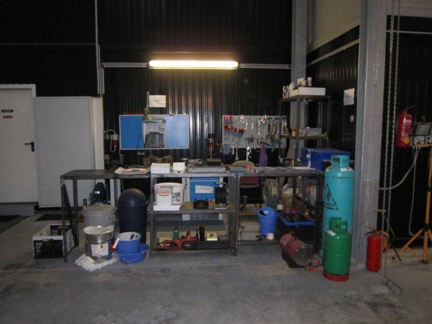 Werkstattbereich mit Regalen, Werkzeugen, Gasflaschen und einer Arbeitsfläche.